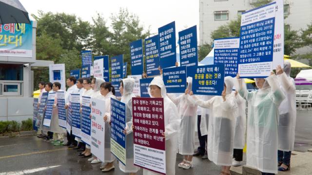전능하신 하나님 교회 크리스천들이 온수 교회 입구에서 피켓을 들고 가족을 이용하여 허위 시위를 벌이고 있는 중국 공산당에 항의하고 있다.