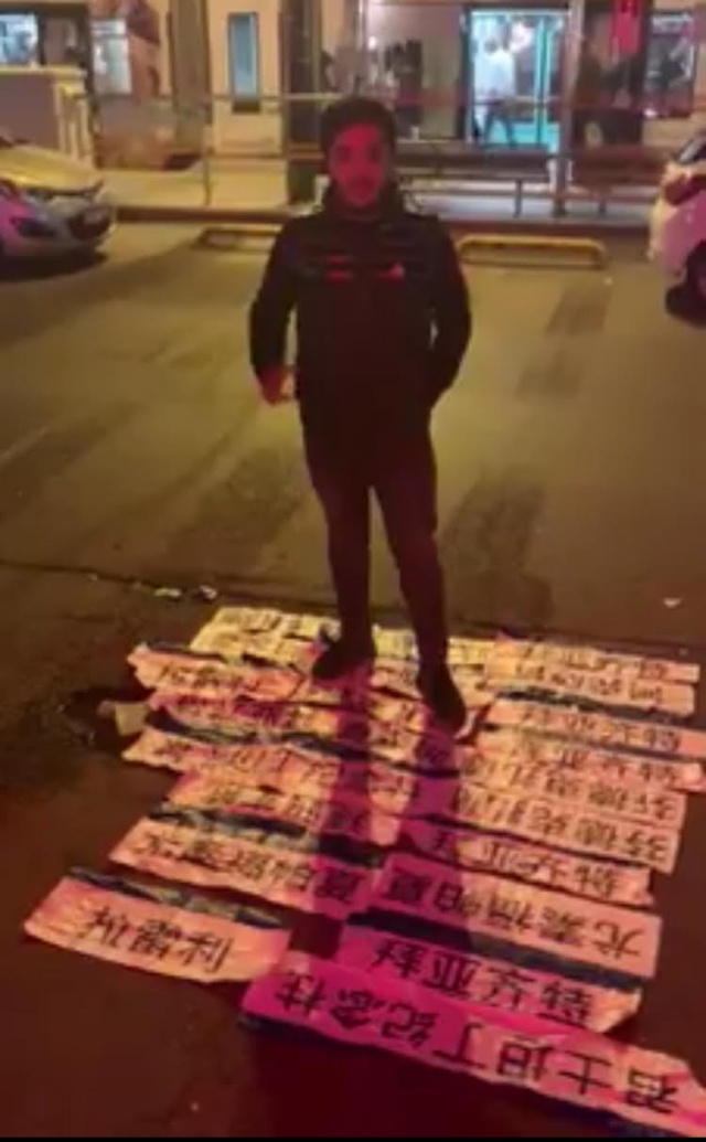 어느 위구르인 젊은이가 터키인 지지자들과 함께 하룻밤 사이에 제거한 전차역들의 중국어 정차 표기들을 밟고 서서 포즈를 취한 모습
